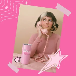 Pink “Just Vibin’” tumbler on a table beside a woman holding a pink retro phone, framed in a Y2K, style pink graphic background.
