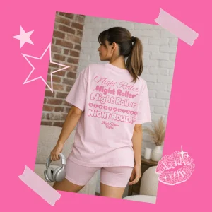 Model wearing a light pink Night Roller oversized tee with “Night Roller” back print, holding silver headphones (Pretty In Print tee).