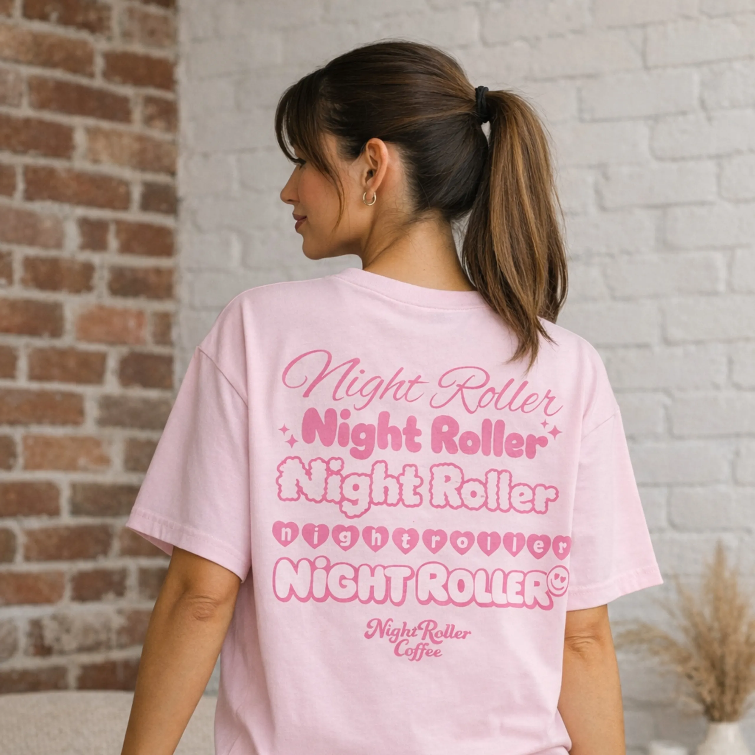 Back view of model wearing a light pink Night Roller oversized t-shirt with layered “Night Roller” retro back print.